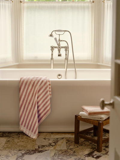 Bathroom with a bathtub, striped towel, and wooden stool.