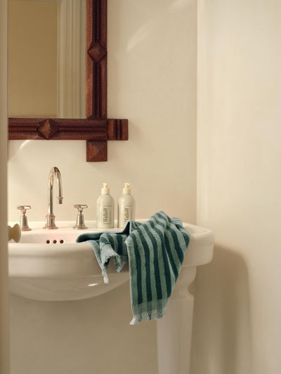 Bathroom sink with a towel and bottles under a wooden-framed mirror.
