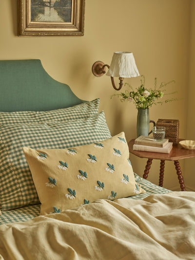 Bedroom with green headboard, checkered pillows, and a small table with a lamp and flowers.