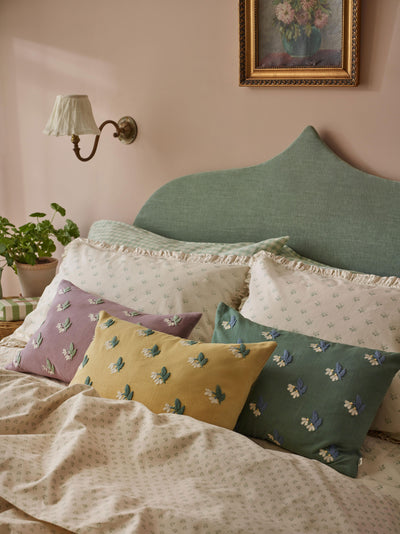 Colorful pillows on a bed with a decorative wall lamp and framed picture in the background.