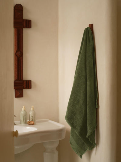 Bathroom with a green towel hanging on a wooden rack, a sink with bottles, and a mirror.
