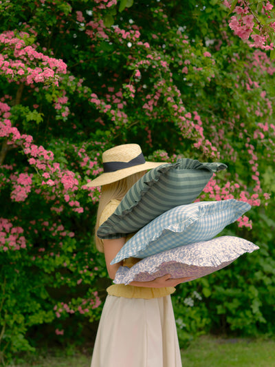 Person holding three decorative pillows against a floral background