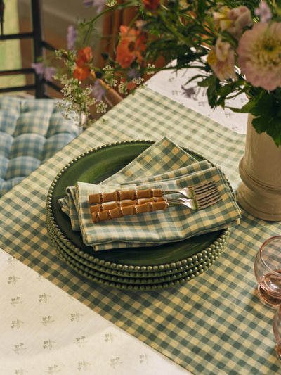 Green checkered tablecloth with plates, napkins, and flowers on a table.