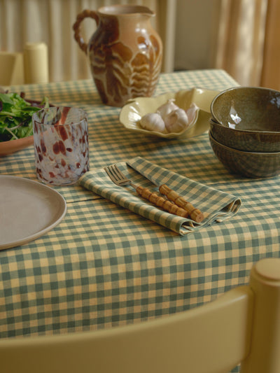 Dining table setting with checkered tablecloth, ceramicware, and cutlery.