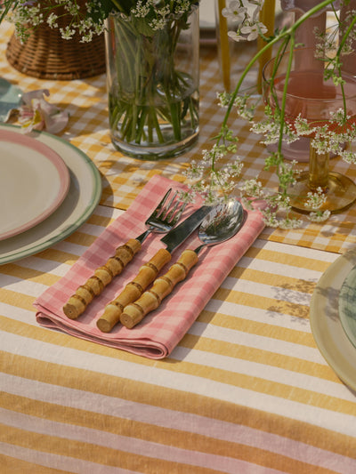 Table setting with striped tablecloth, pink checkered napkin, and floral decorations.