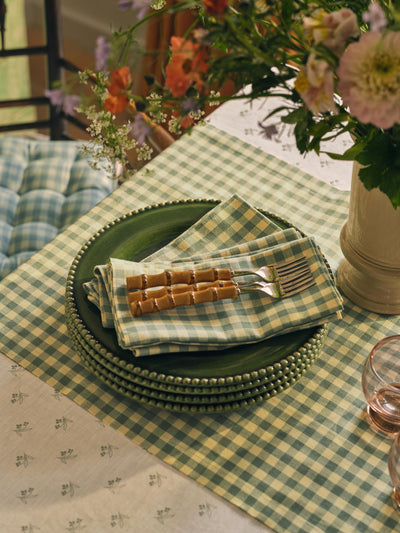 Green checkered tablecloth with plates, napkins, and flowers on a table.